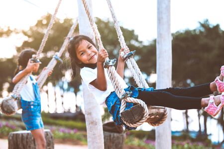 Happy asian child girl having fun to play on wooden swings with her sister in playground with beautiful natureの写真素材