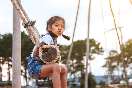 Happy asian child girl having fun to play on wooden swings in playground with beautiful natureの写真素材