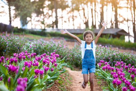 Cute asian child girl raise their arms and run in the flower garden with freshness and happinessの写真素材