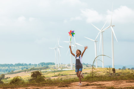 Cute asian child girl is running and playing with wind turbine toy  with fun in the wind turbine fieldの写真素材