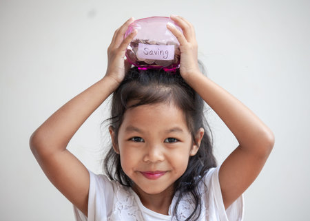 Cute asian child girl holding piggy bank and putting money into piggy bank to save money for the futureの写真素材