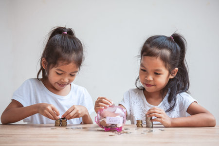 Two cute asian child girls putting money into piggy bank to save money for the future together with fun and happinessの写真素材