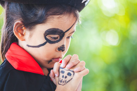 Cute asian child girl wearing halloween costumes and makeup making hands folded in prayer on...
