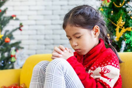 Cute asian child girl closed her eyes and folded her hand in prayer to wish in Christmas celebrationの写真素材