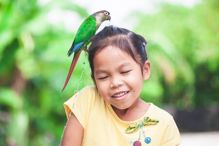 Beautiful little parrot birds standing on child head. Asian child girl play with her pet parrot bird with funの写真素材