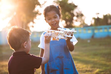 Two asian child girl and boy playing with toy wooden airplane in the park together at sunset time with funの写真素材