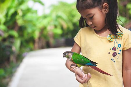 Beautiful little parrot birds standing on child hand. Asian child girl play with her pet parrot bird with funの写真素材
