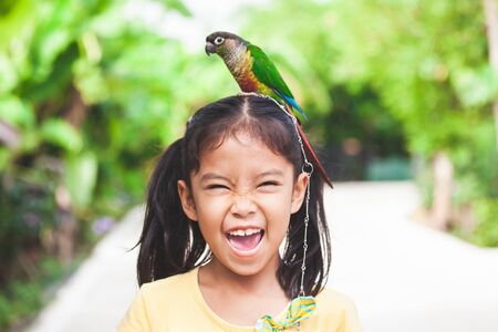 Beautiful little parrot birds standing on child head. Asian child girl play with her pet parrot bird with funの写真素材