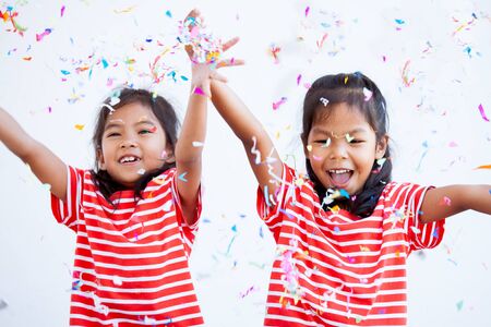 Cute asian child girl and her sister play with colorful confetti together to celebrate in their party with funの写真素材