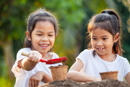 Two asian child girls prepare soil for planting young seedlings in recycle fiber pots together in the garden with funの写真素材