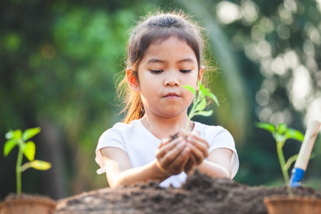 Cute asian child girl holding young tree for planting in the black soil in the garden with funの写真素材