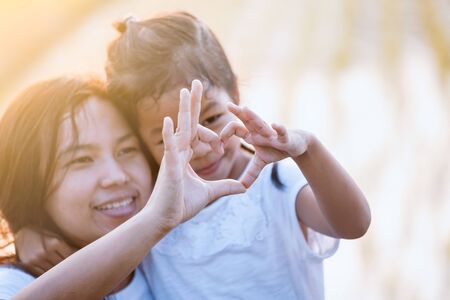 Asian mother and daughter making heart shape with hands together with love in the field with sunlightの写真素材