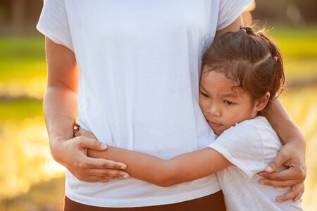 Sad asian child girl hugging her mother  in the paddy field with the sunlightの写真素材