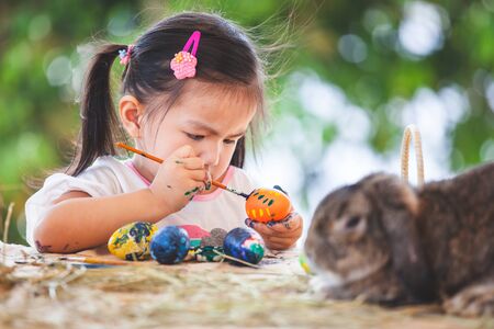 Cute asian child girl drawing and painting on easter eggs prepare for easter day. Child and Holland lop rabbit in easter festive.の写真素材