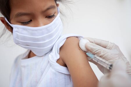 Doctor injecting vaccination on asian child girl arm. The child girl wearing protection mask for protect air smog pollution with PM 2.5 and Covid-19 virus. Healthy and medical concept.の写真素材