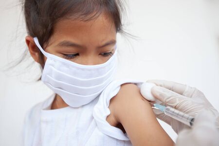 Doctor injecting vaccination on asian child girl arm. The child girl wearing protection mask for protect air smog pollution with PM 2.5 and Covid-19 virus. Healthy and medical concept.の写真素材