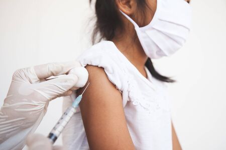 Doctor injecting vaccination on asian child girl arm. The child girl wearing protection mask for protect air smog pollution with PM 2.5 and Covid-19 virus. Healthy and medical concept.の写真素材