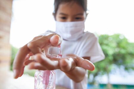 Asian child girl wearing protection mask for protect air smog pollution with PM 2.5 and Covid-19 virus and using disinfectant gel wash her hand to prevent contamination by virus and bacteria. Healthy and medical concept.の写真素材