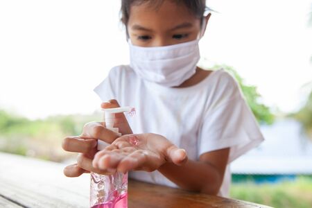 Asian child girl wearing protection mask for protect air smog pollution with PM 2.5 and Covid-19 virus and using disinfectant gel wash her hand to prevent contamination by virus and bacteria. Healthy and medical concept.の写真素材