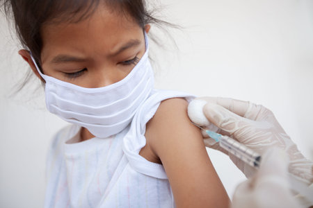 Doctor injecting vaccination on asian child girl arm. The child girl wearing protection mask for...