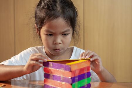 Asian child girl glueing colored ice cream sticks by hot melt electrical glue gun. Children have fun to make house on a handicraft project.の写真素材