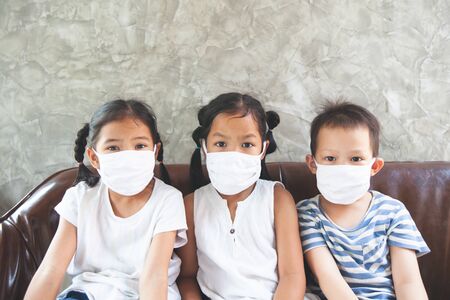 Asian children boy and girls wearing protection mask playing on the smartphone together at home quarantine from the coronavirus Covid-19 and air pollution pm2.5.の写真素材
