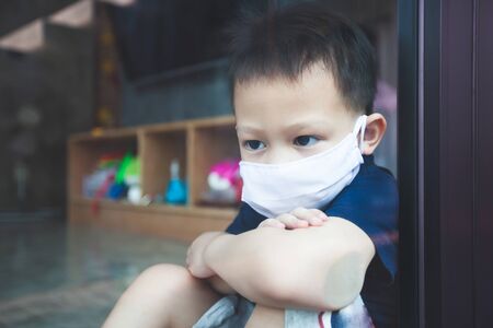 Asian child boy wearing protection mask looking outside through the window and stay at home quarantine from the coronavirus Covid-19 and air pollution pm2.5.の写真素材