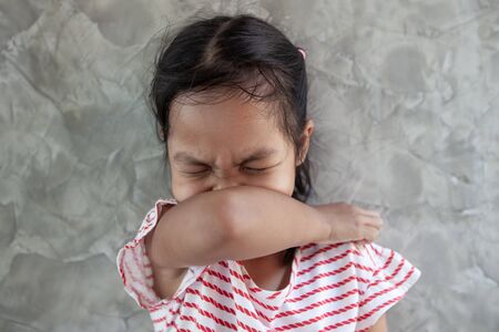 Asian child girl sneezing on hinge joints arm for protect from virus and stop coronavirus covid19 outbreak. She stay at home quarantine from the coronavirus Covid-19 and air pollution pm2.5.の写真素材