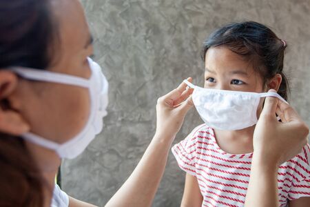 Asian mother help her daughter wearing protection mask to protect the coronavirus Covid-19 outbreak situation and air smog pollution with PM 2.5の写真素材
