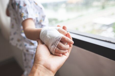 Parent hand holding sick son hand who have IV solution bandaged with love and care  while he looking outside through the window and want to go homeの写真素材