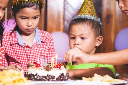 Asian children girls and boys lighting candle on birthday cake together in birthday partyの写真素材