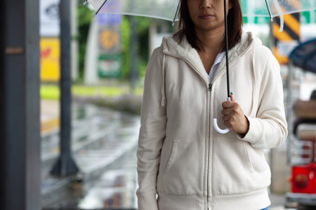 Asian woman holding umbrella while waiting taxi and standing on the city sidewalk street in the...