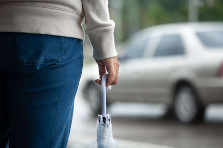 Asian woman holding umbrella while waiting taxi and standing on the city sidewalk street in the rainy day.の写真素材