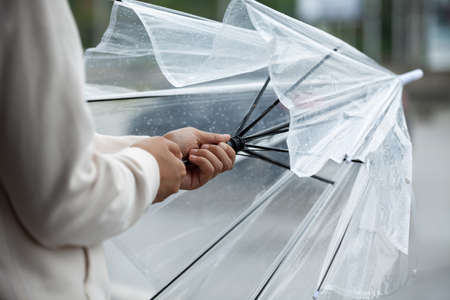Asian woman opening closing an umbrella while waiting taxi and standing on the city sidewalk street in the rainy day.の写真素材