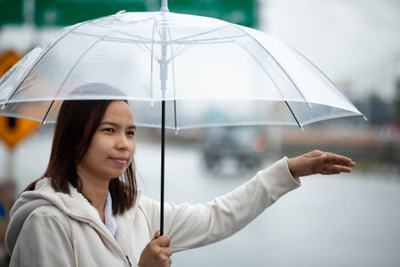 Asian woman holding umbrella hitchhiking taxi at city street in the rainy day.