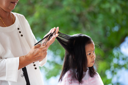 Cute asian child girl getting haircut by grandmother at home