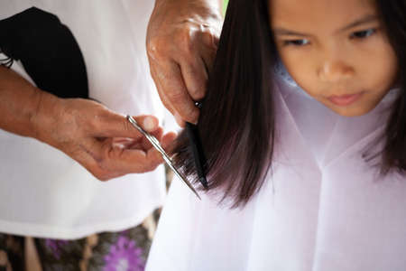 Cute asian child girl getting haircut by grandmother at homeの写真素材