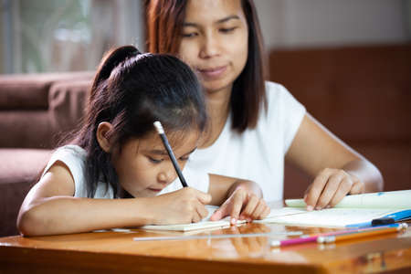 Young asian mother helping her daughter do her homework at home. Education from home concept.の写真素材
