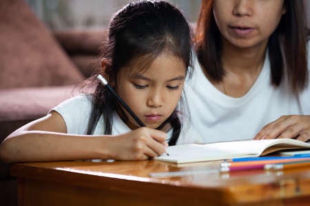 Young asian mother helping her daughter do her homework at home. Education from home concept.の写真素材