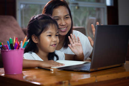 Asian child girl using notebook to learning online technology with her mother to advise beside. Concept of online education, social distance learning at home during quarantine and school holidays.の写真素材
