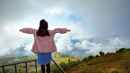 Back view of asian child girl wearing sweater raise her arms looking at the beautiful mist and mountain with freshness and happinessの写真素材