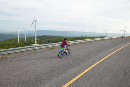 Asian child girl riding bicycle and playing in the wind turbine field with funの写真素材
