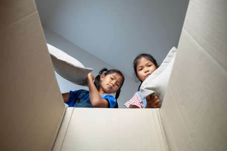 Two asian child girls helping parents put on stuff into the box on moving day. Home renovation and relocation concept.の写真素材