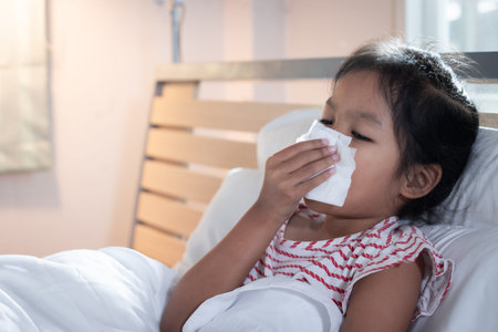 Asian child girl get sick ,coughing and sneezing. She is wiping nose with paper tissues. Sick child...