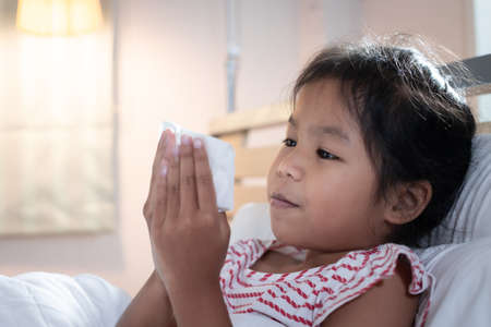 Asian child girl get sick ,coughing and sneezing. She is wiping nose with paper tissues. Sick child and health care concept.の写真素材