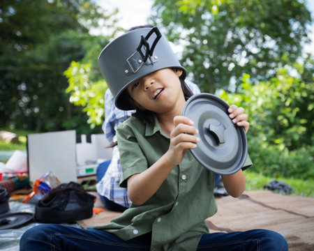 Happy asian child girl put a pot cover on head and having fun to help her parent cooking while...