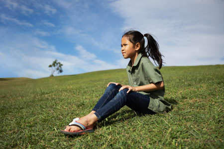 Asian child girl sitting on the hill with green grass to enjoy with beautiful nature in the summer time.の写真素材