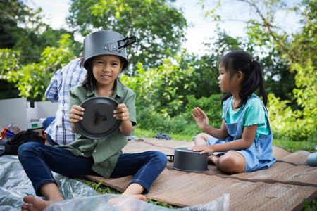 Happy asian child girl put a pot cover on head and having fun to help her parent cooking while...