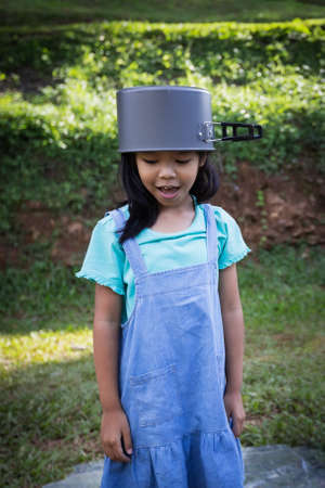 Happy asian child girl put a pot cover on head and having fun to help her parent cooking while family camping.の写真素材