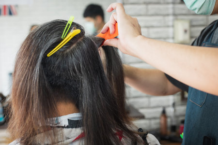 Asian young man being cut from long hair to short hair with scissor by professional barber in...